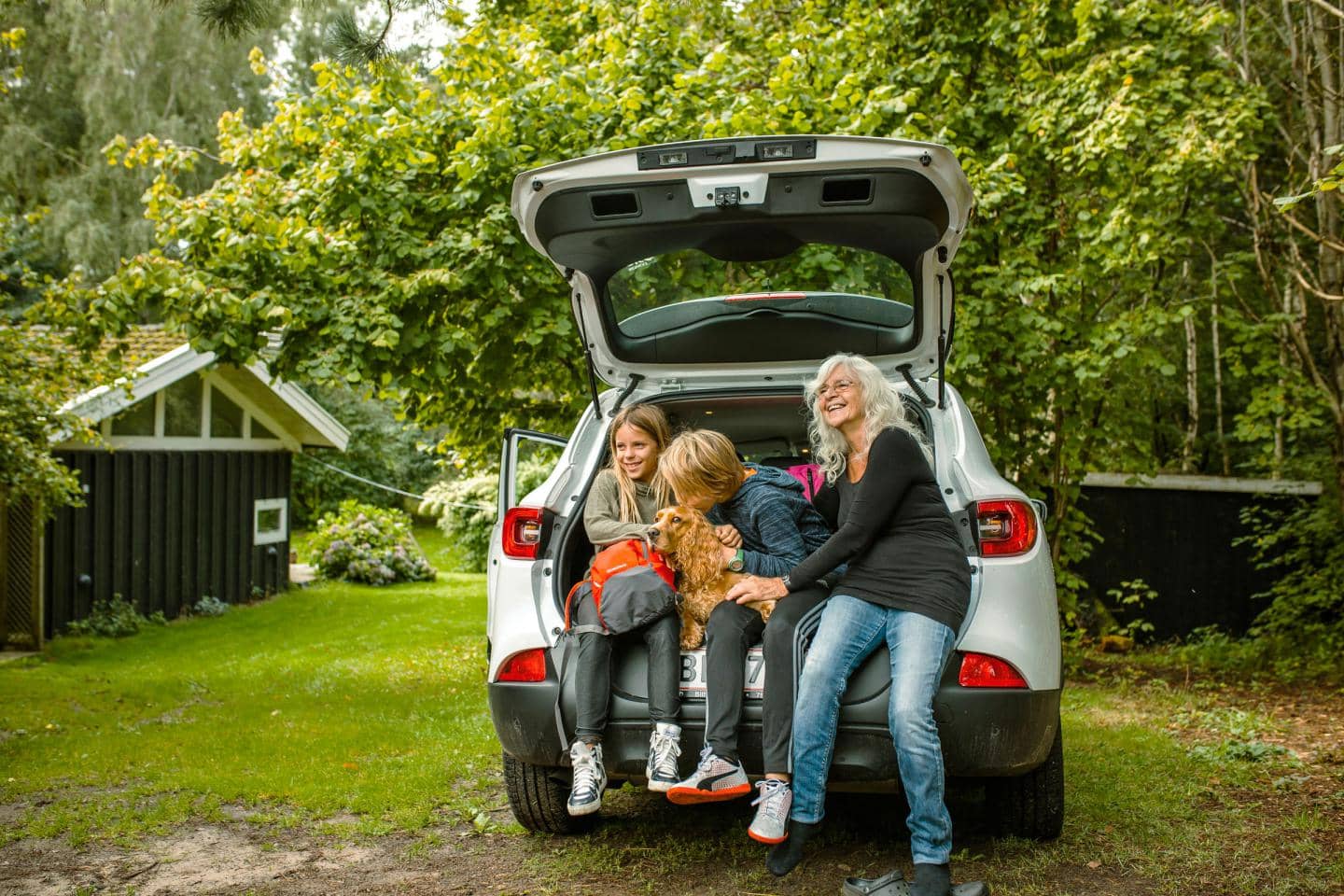 Bedstemor og børn sidder i bagagerum af bil, fotografi