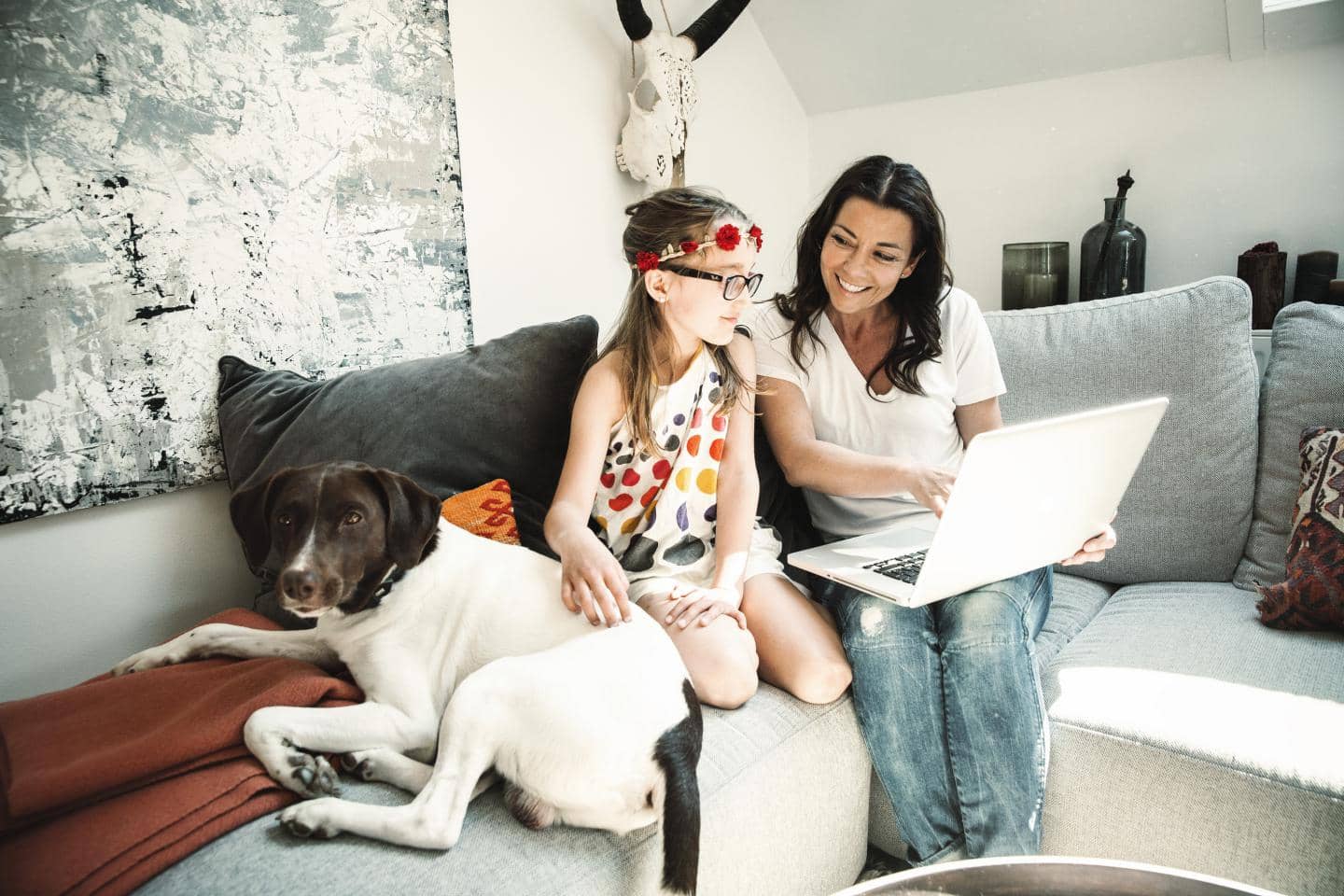 Mor og datter sidder i sofa og kigger på computer imens de smiler