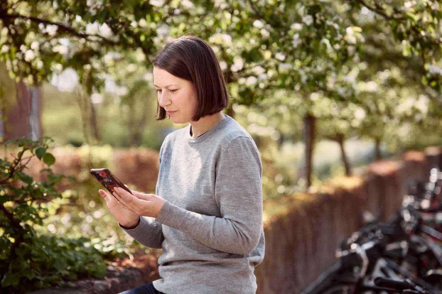 Kvinde står under træer og kigger på sin telefon